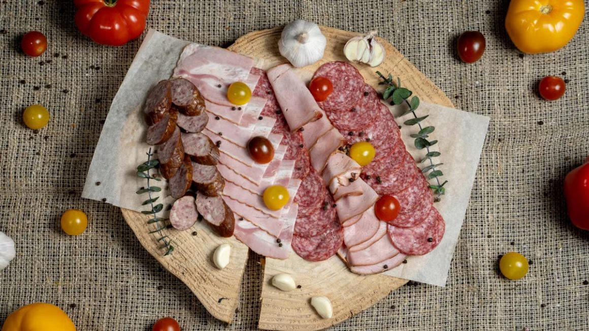 A high-angle view of assorted cured meats and fresh tomatoes on a rustic wooden board.
